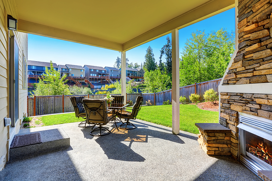 cozy covered patio with stone trim fireplace. glass top patio table and comfortable chairs with stripped covers